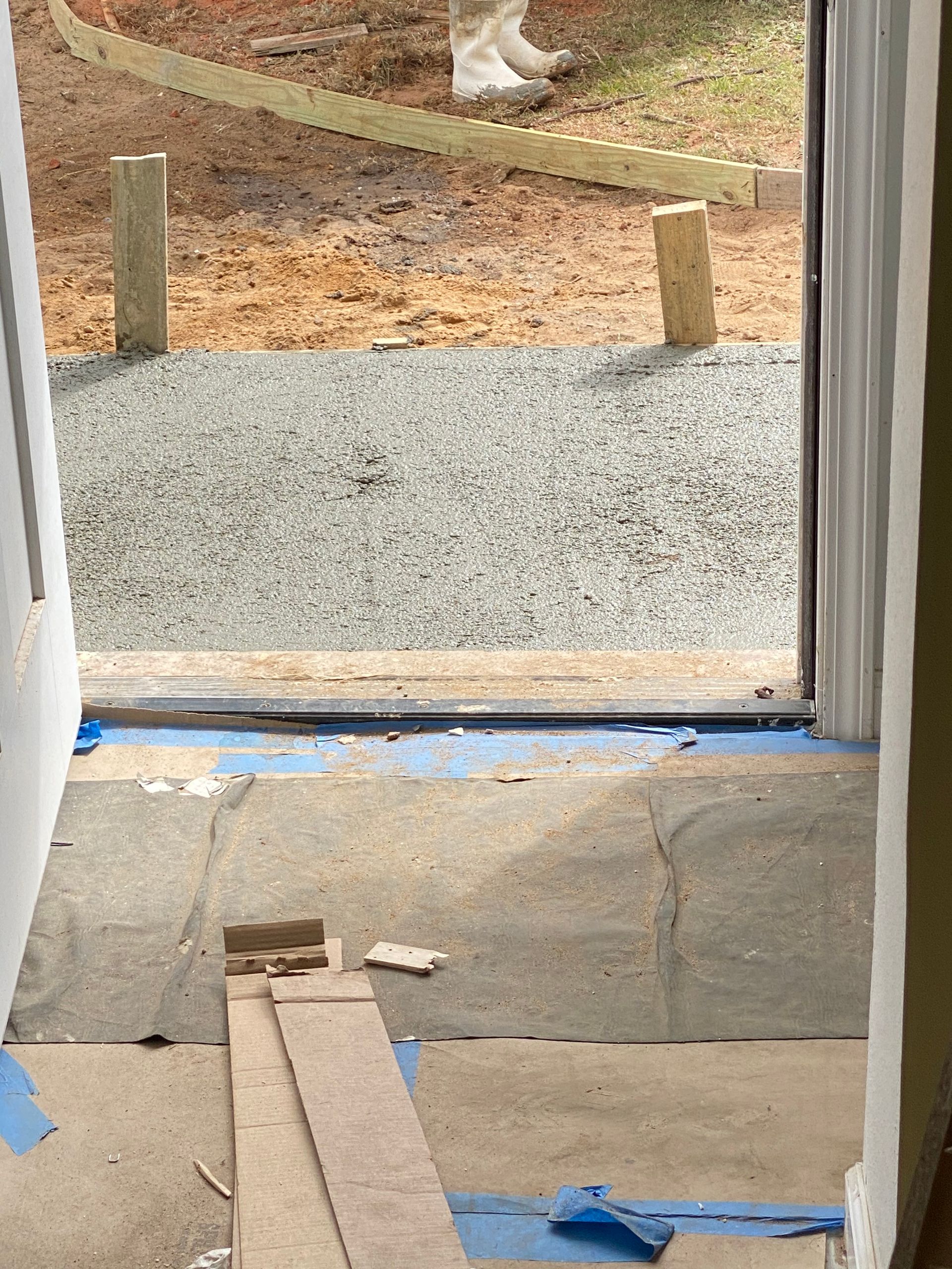 Doorway with a wooden ramp and blue tape leading to a gravel path outside.