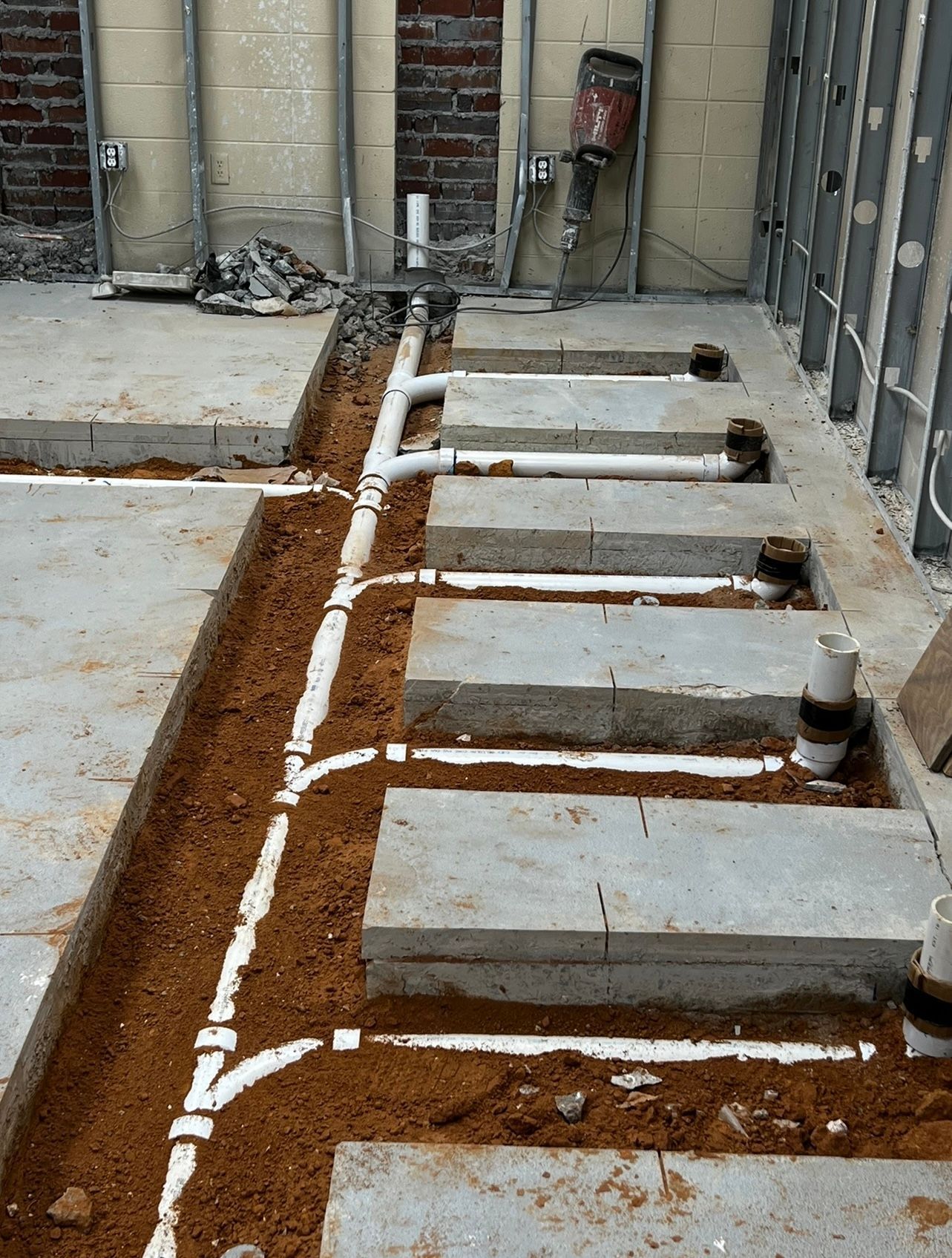 White utility pipes laid in brown soil beside concrete foundation walls at a construction site
