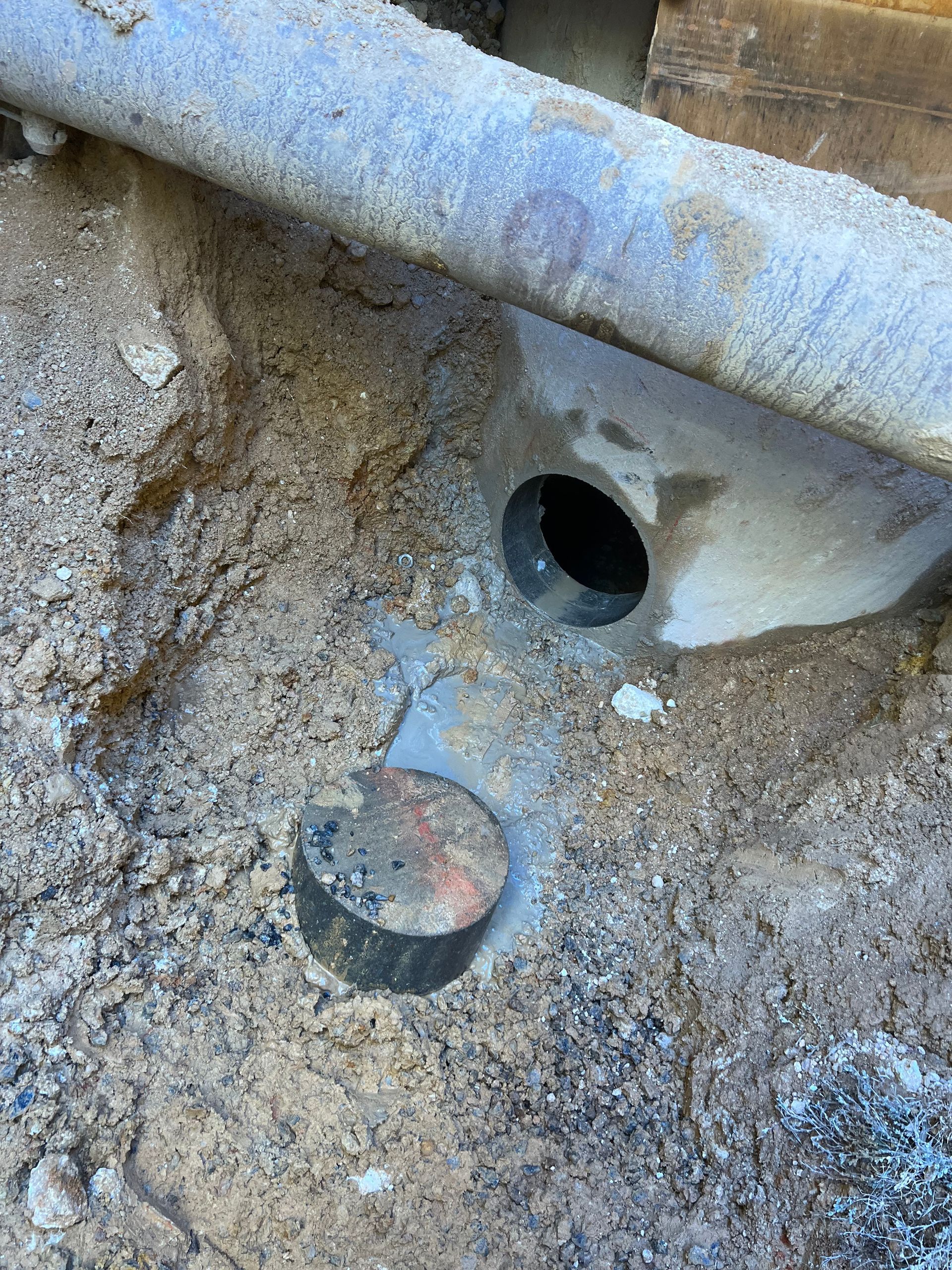 Close-up of a rusty metal pipe and hole in dirt and concrete debris