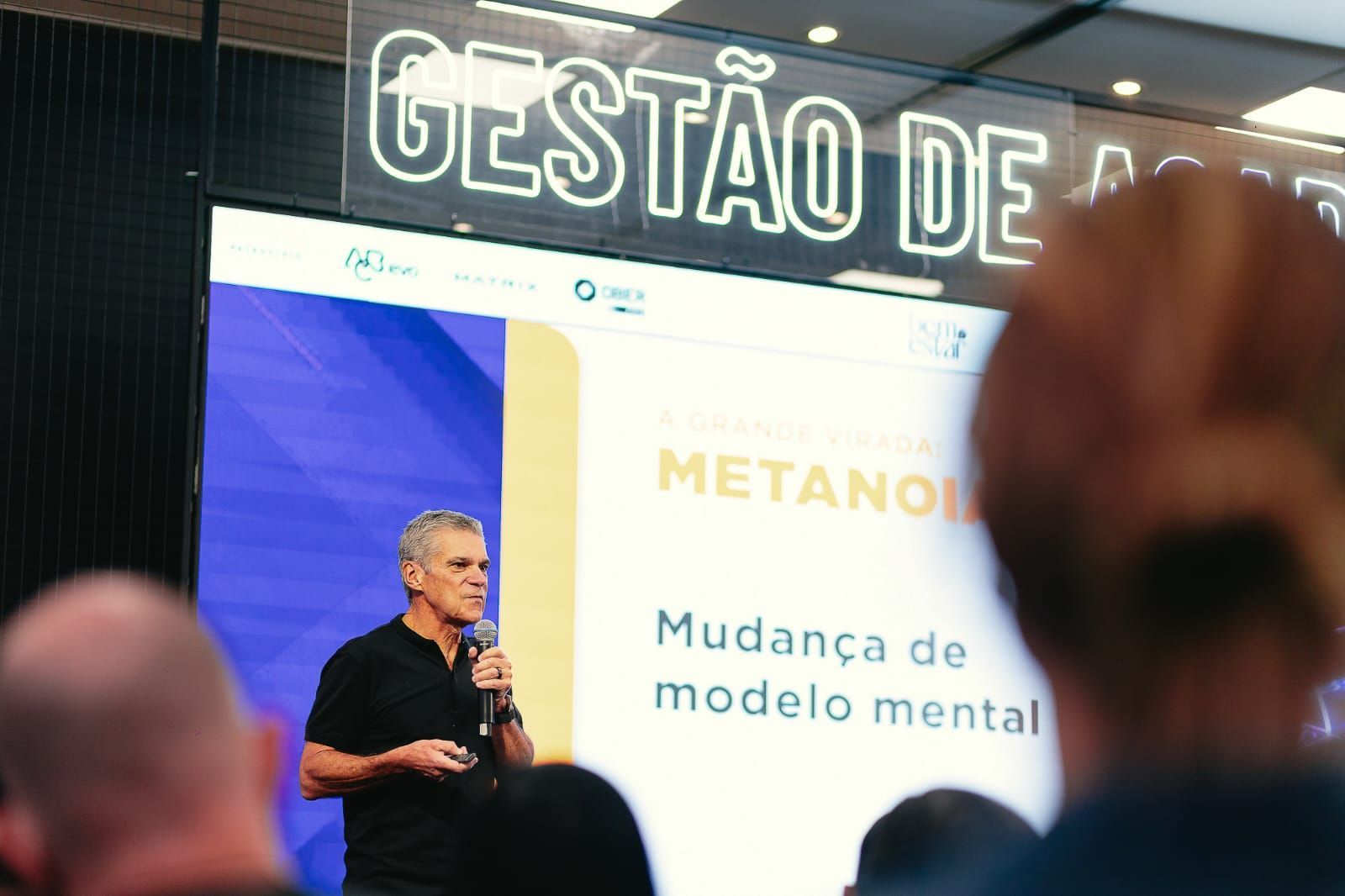 Homem discursando em uma conferência. Texto na tela: 