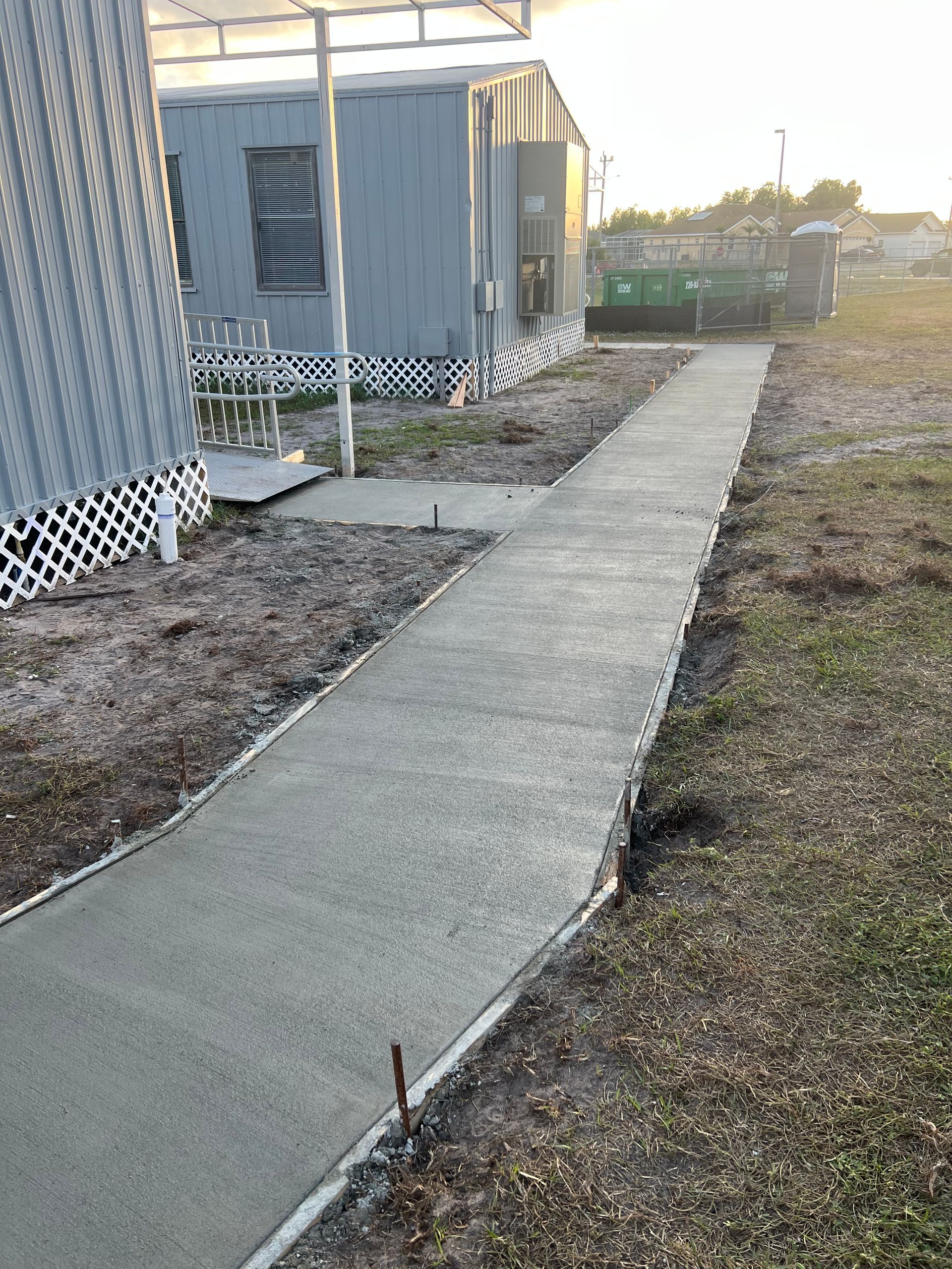 Newly poured concrete sidewalk leading past modular buildings.