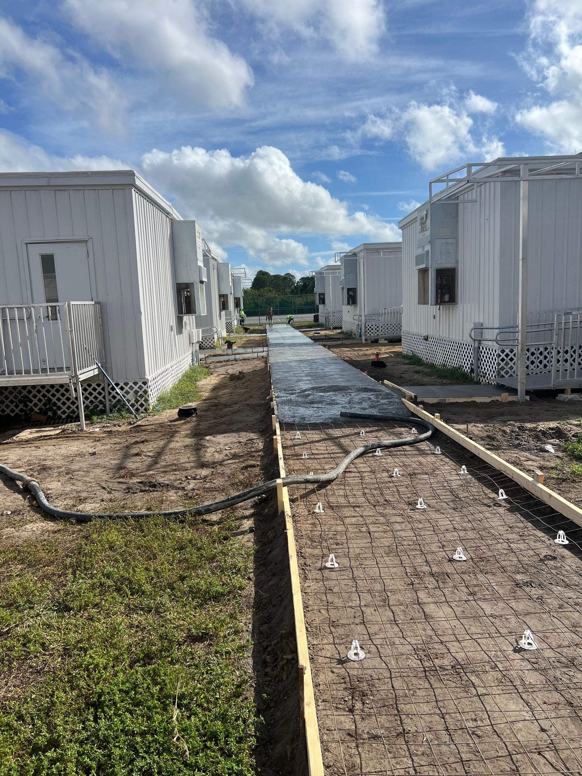 Row of white modular buildings with a narrow path in between, under a cloudy blue sky.