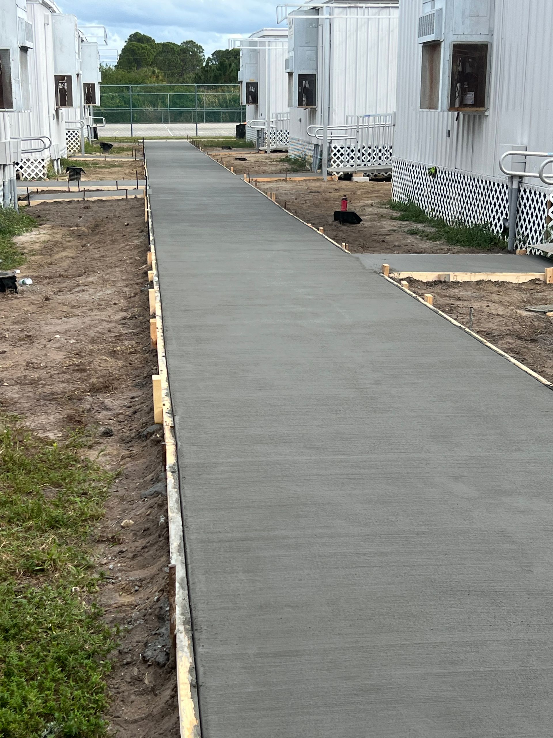 Newly poured concrete pathway between white buildings, construction in progress.