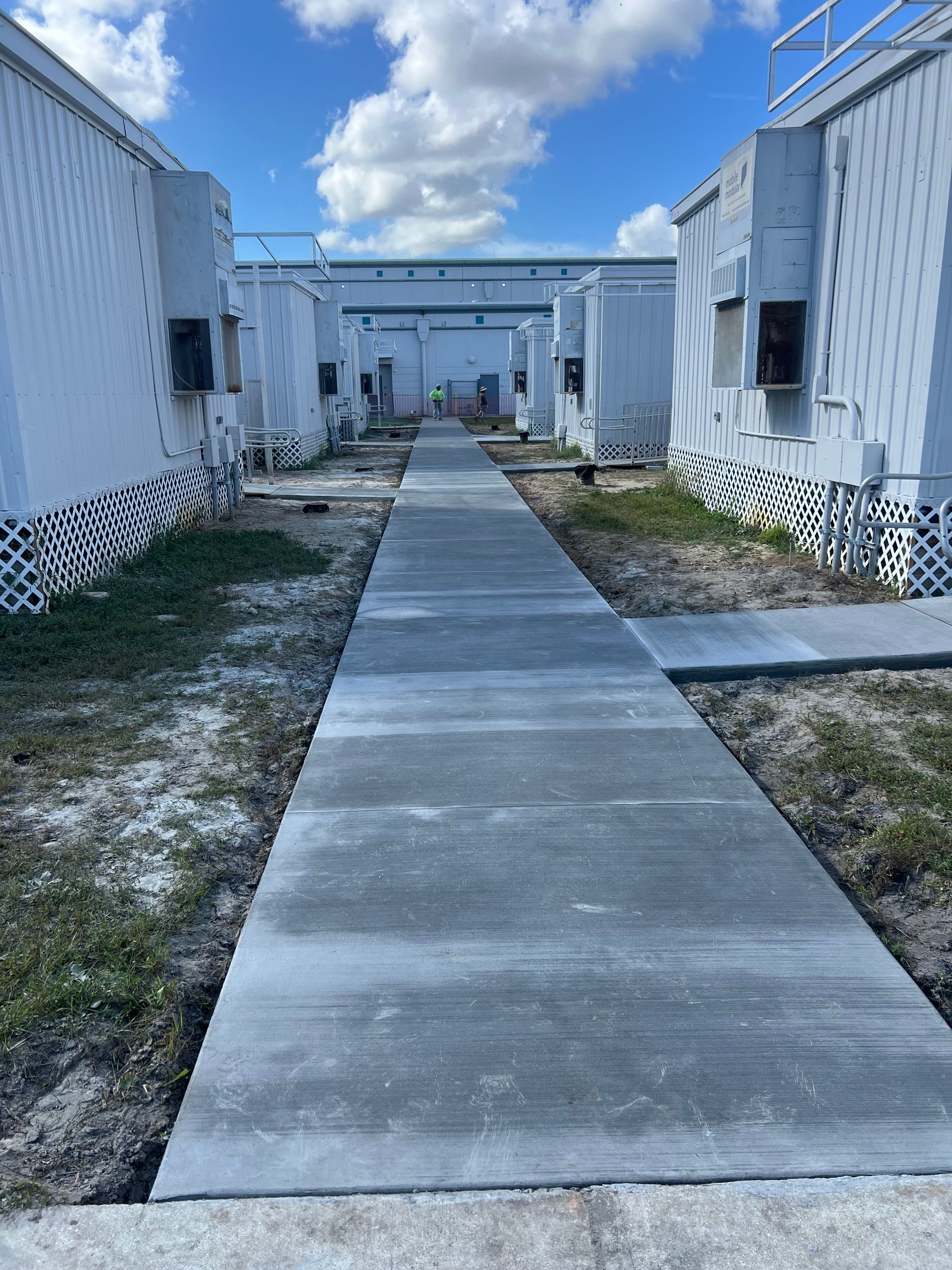 A concrete walkway between rows of white modular buildings on a sunny day.