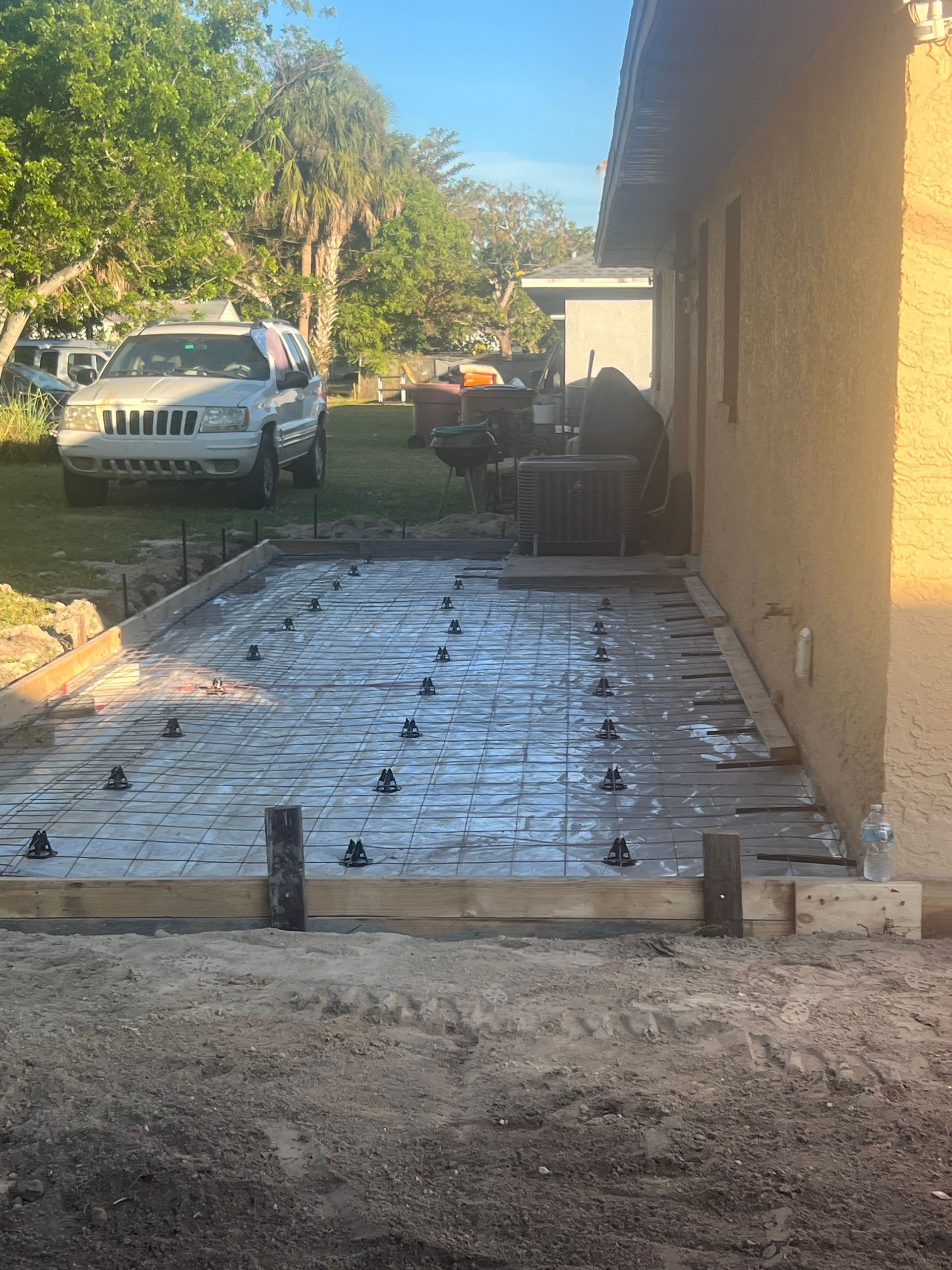Newly poured concrete patio, reinforcing bars and leveling devices visible, next to a beige building.
