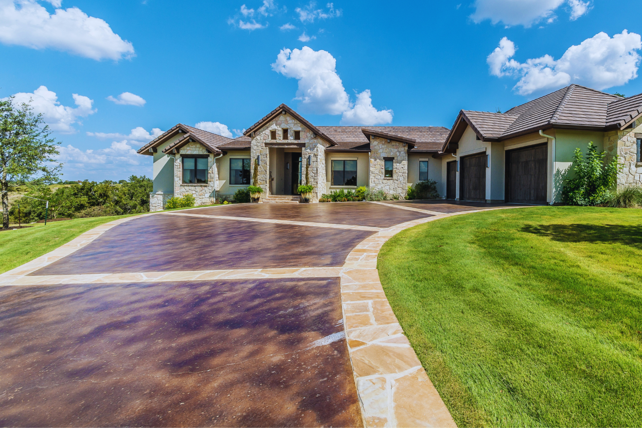 Stone house with brown driveway, green lawn, and blue sky.