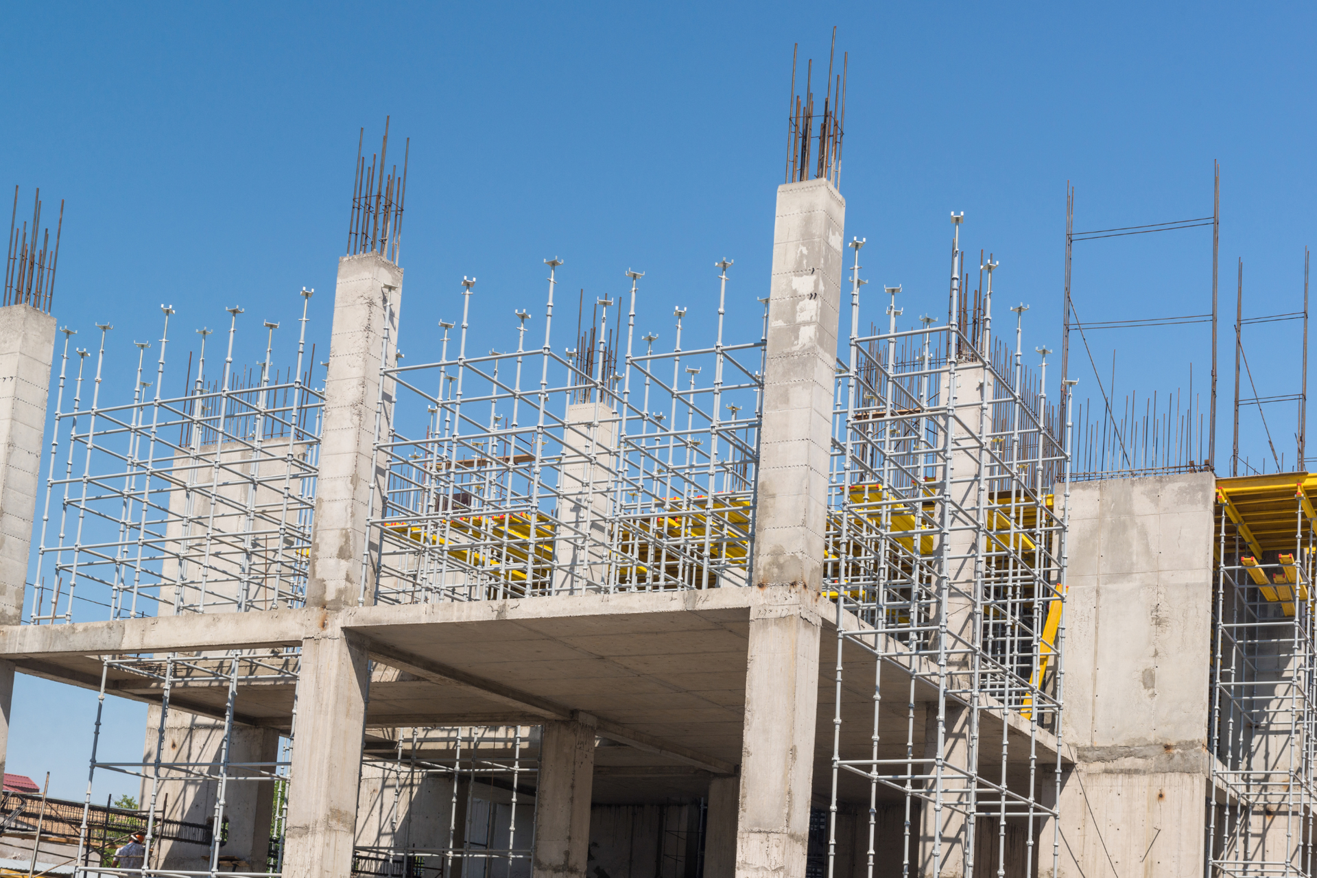 Construction site of a concrete building with rebar columns and scaffolding, against a blue sky.