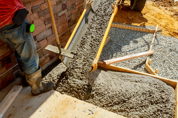 Worker pouring concrete into a wooden frame, creating a walkway.