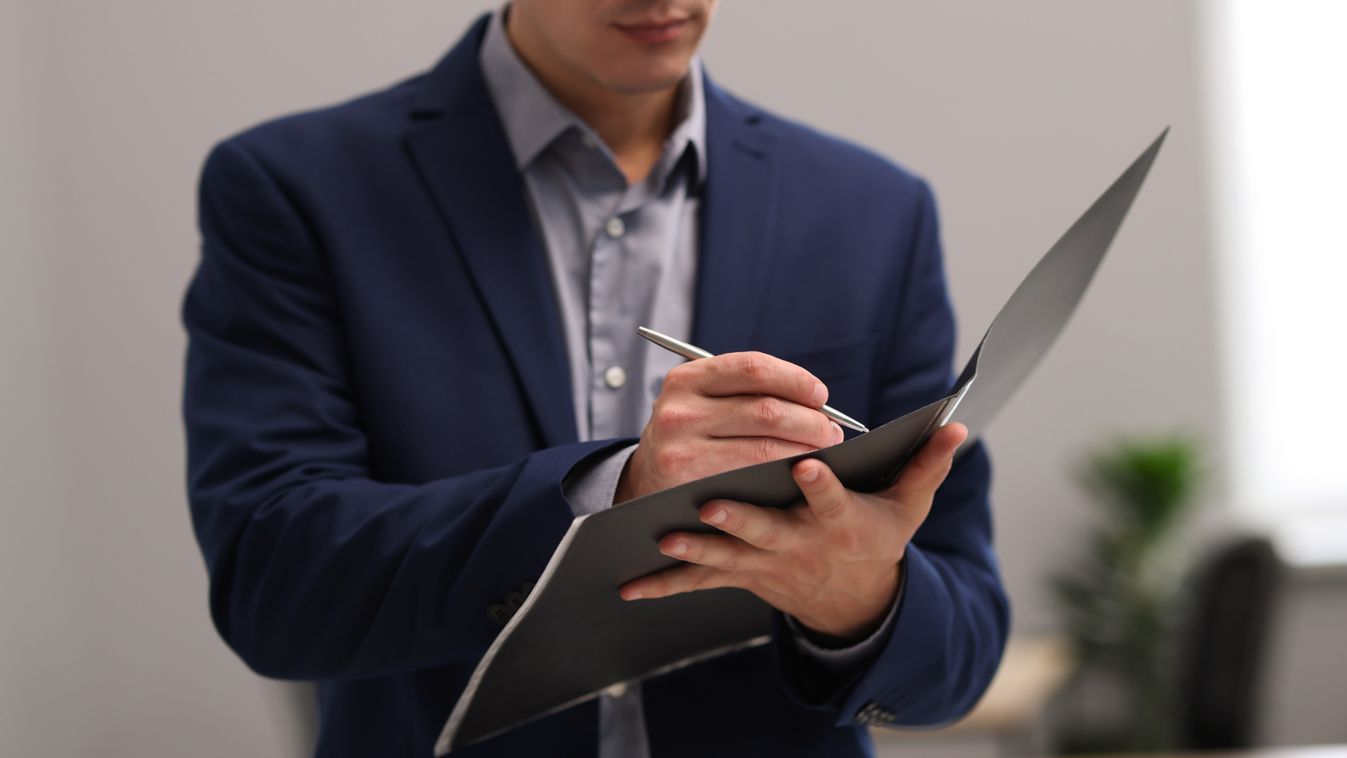 Person in a navy suit taking notes on a clipboard in an office setting