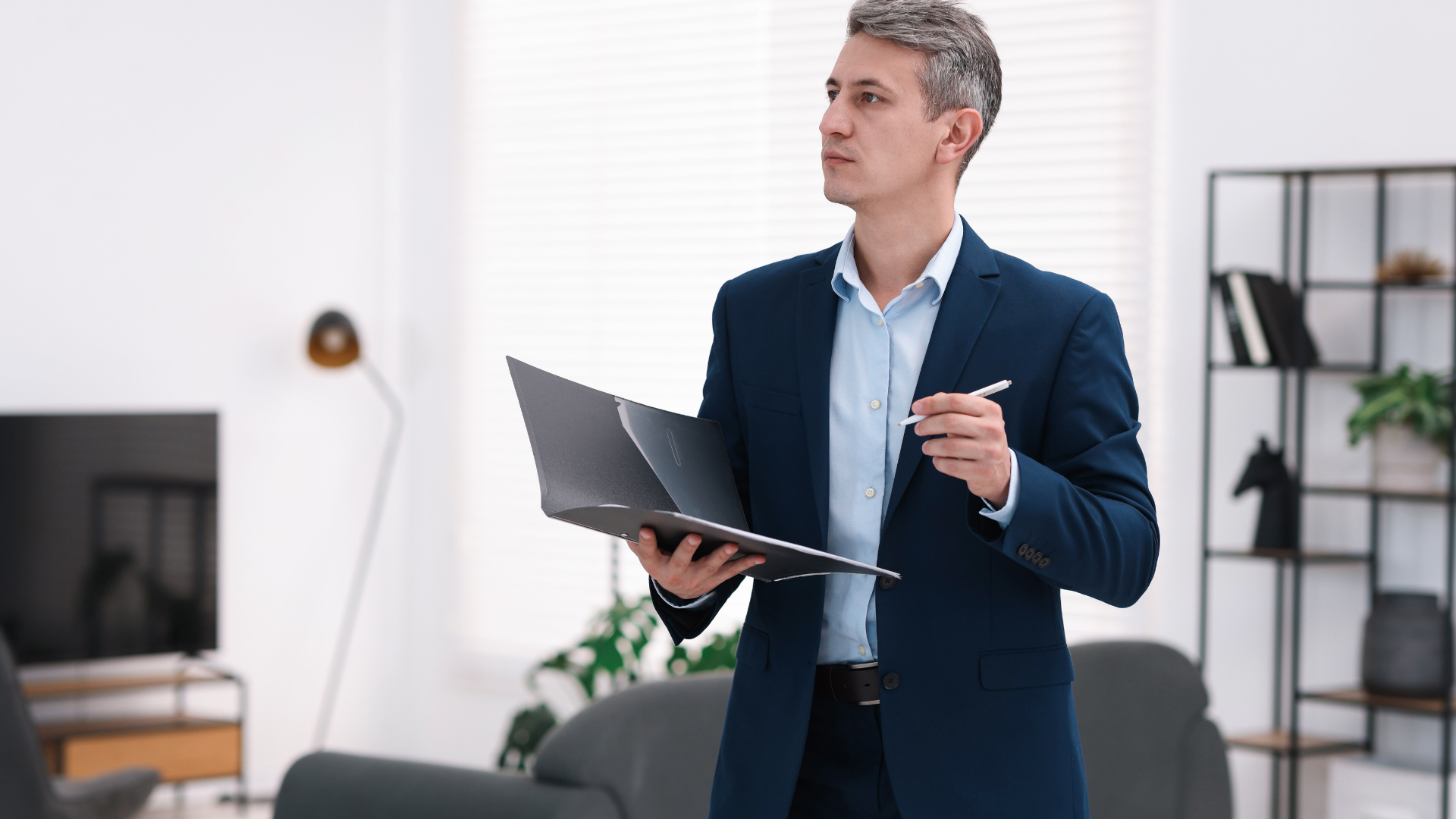 Man in navy blazer holding a laptop and pen in a modern office