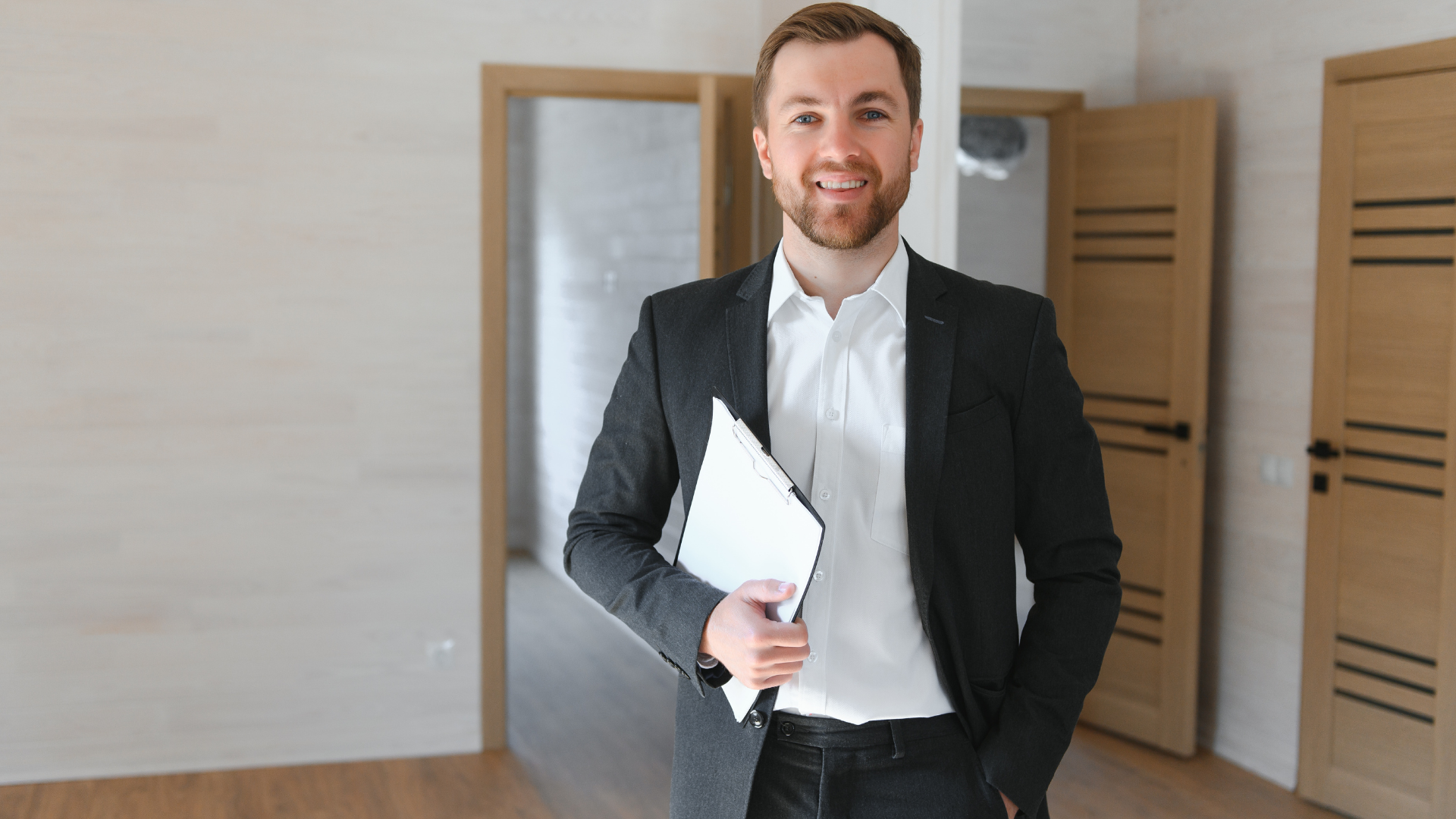 Man in suit holding a clipboard, smiling in front of interior doors.