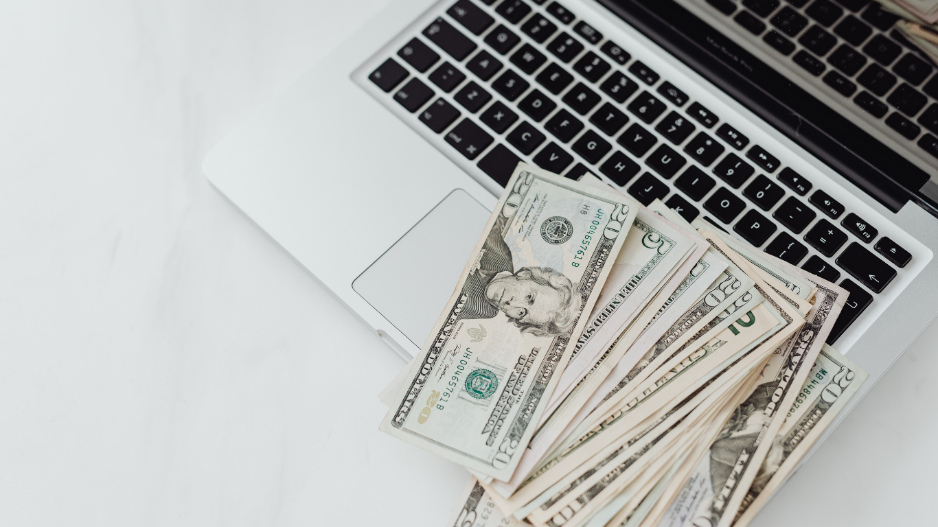 Cash on a white desk beside a laptop keyboard and trackpad.
