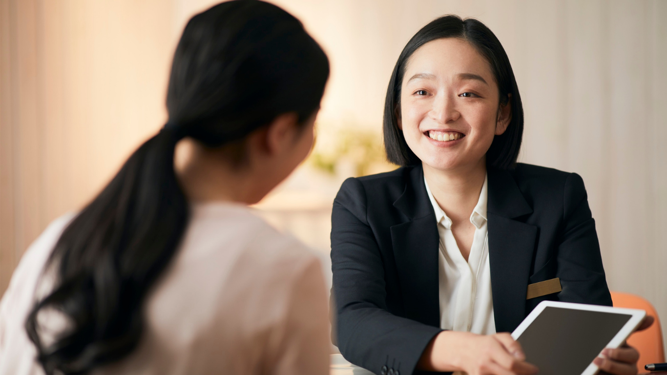 Two women in a meeting, one smiling and holding a tablet across the table.