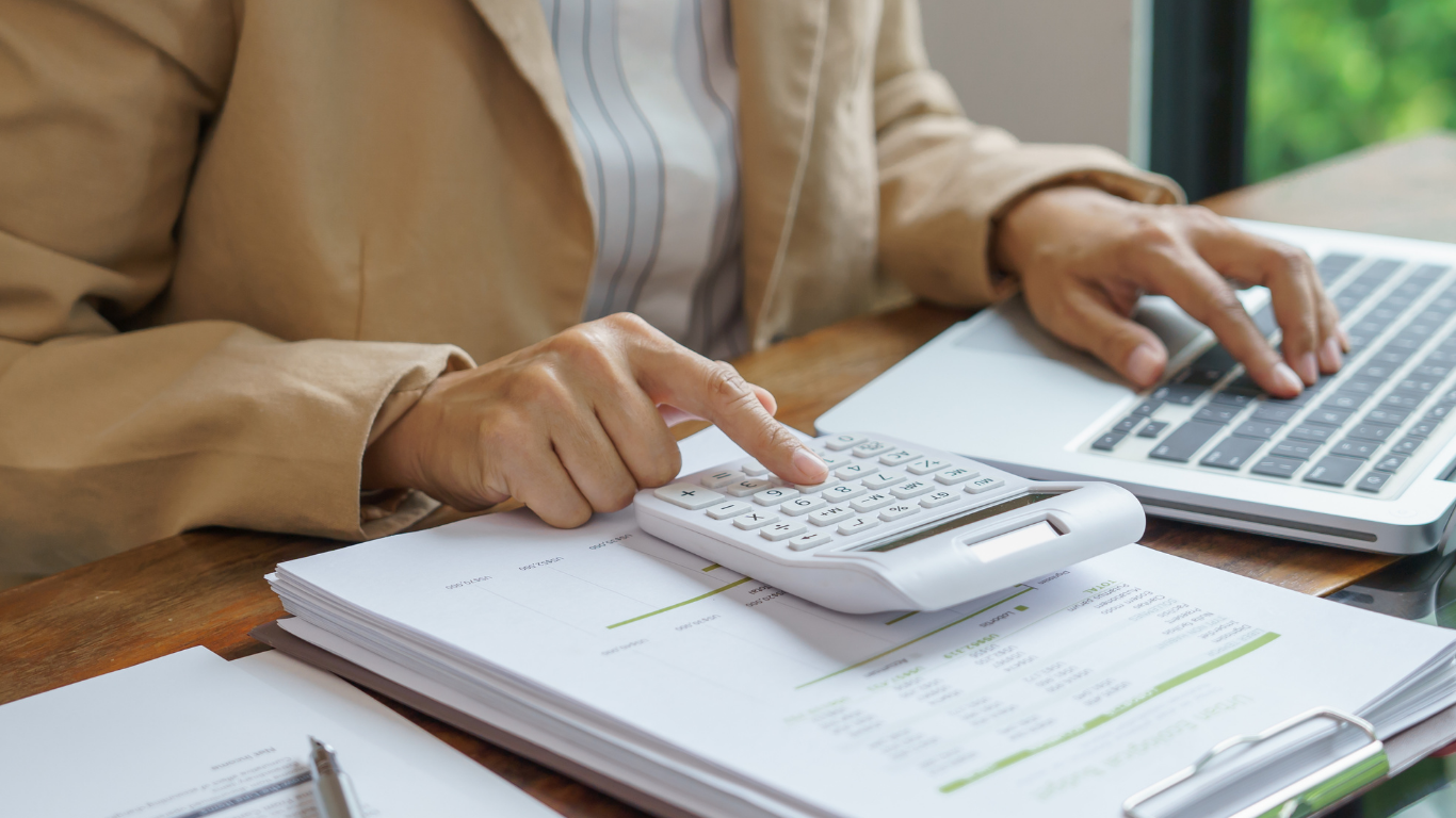 Hands using calculator and laptop over paperwork on a desk