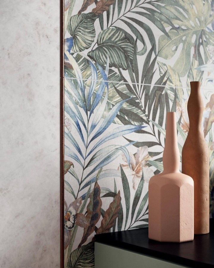 Due vasi in ceramica su una superficie nera, davanti a una carta da parati con motivi di foglie tropicali e a una parete chiara con texture.