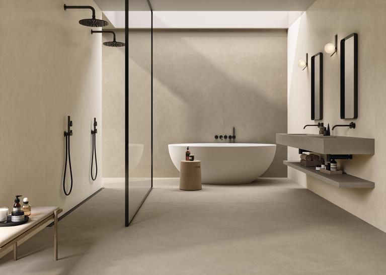 Un bagno minimalista e moderno con doppia doccia, vasca freestanding e doppio lavabo sospeso in cemento nei toni del beige.