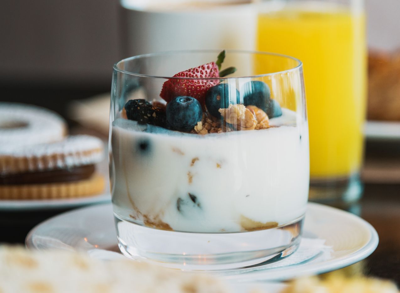 Un vaso de yogur con frutos rojos y granola en un plato.