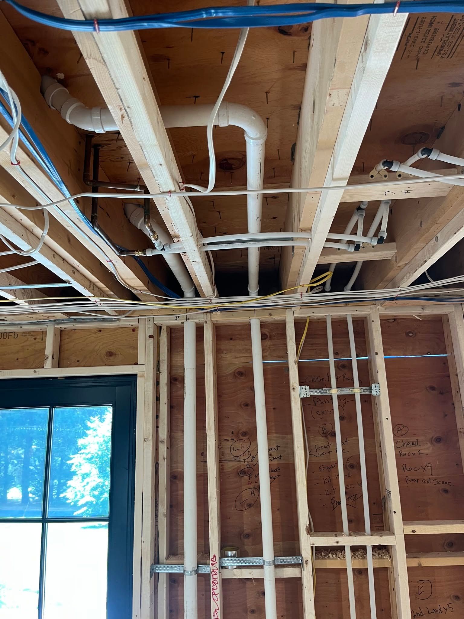 Interior of a house under construction, showing exposed ceiling joists, ducts, and framed walls.