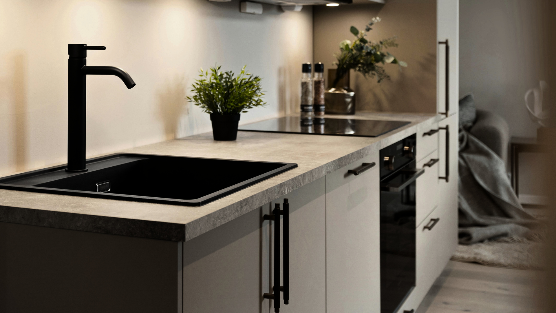 Modern kitchen with black faucet, light countertops, potted plants, and built-in appliances