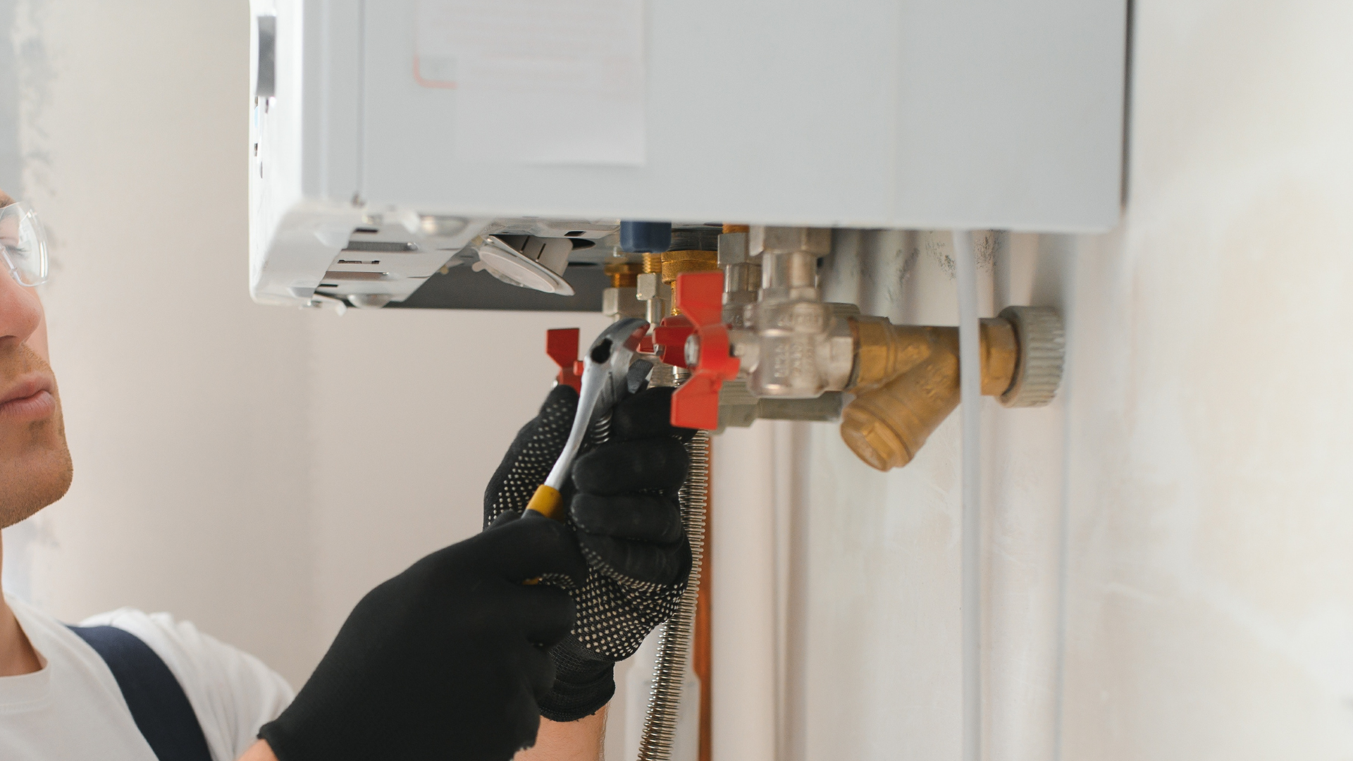 Technician adjusting the valves beneath a wall-mounted boiler with a wrench