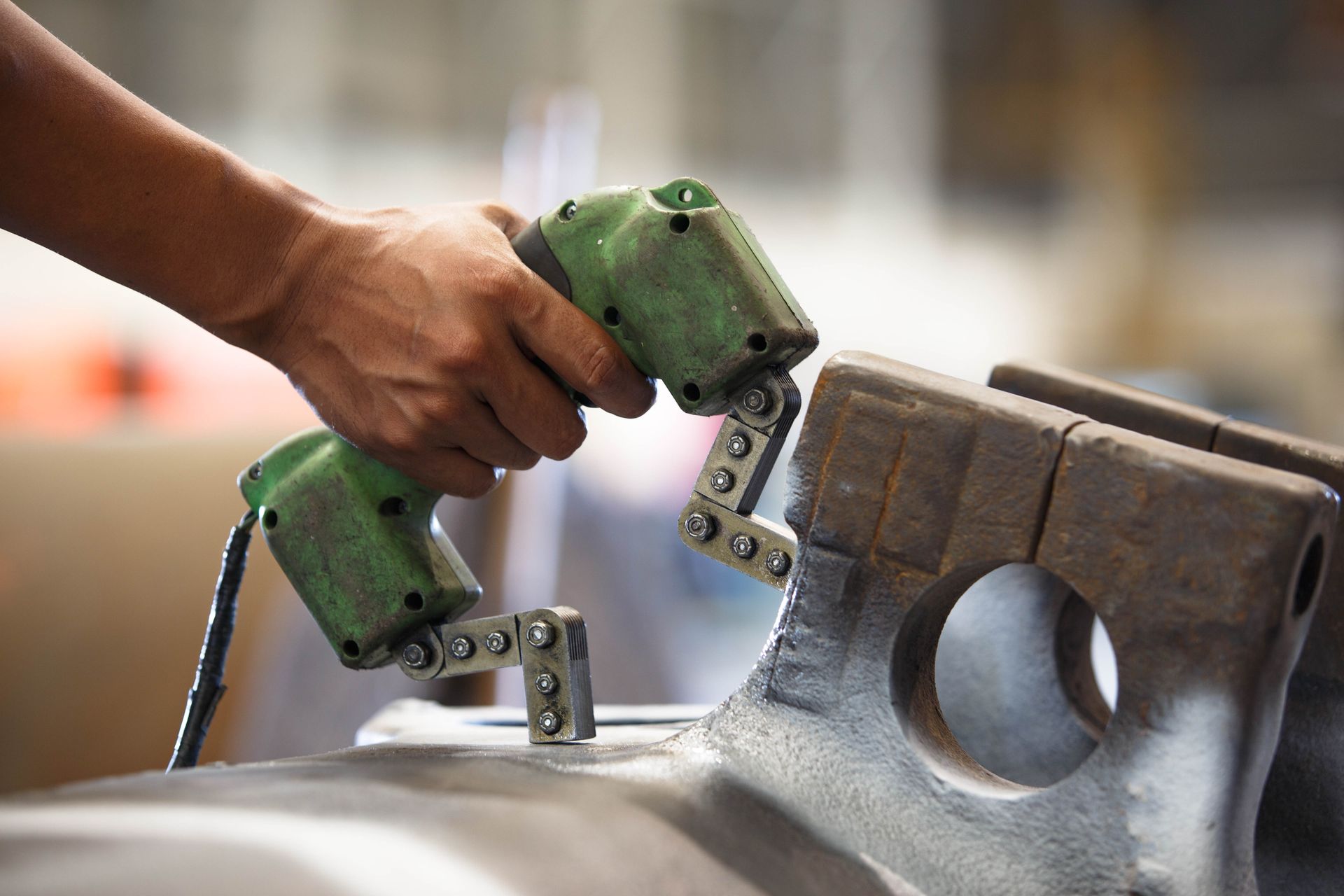 Hand using green power tool to drill metal in a workshop
