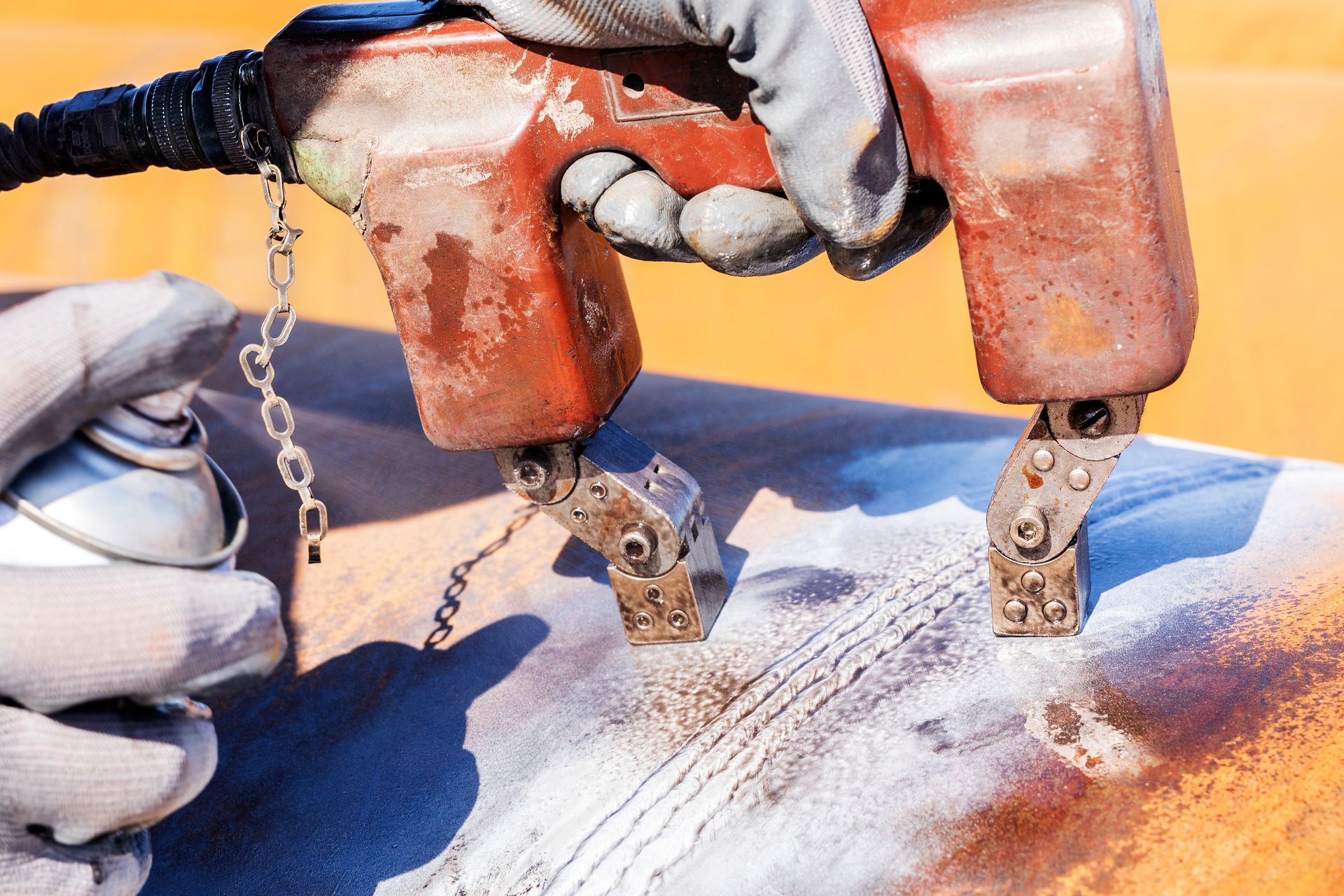 Person using magnetic particle inspection tool on a metal pipe; white coating sprayed, orange and gray.