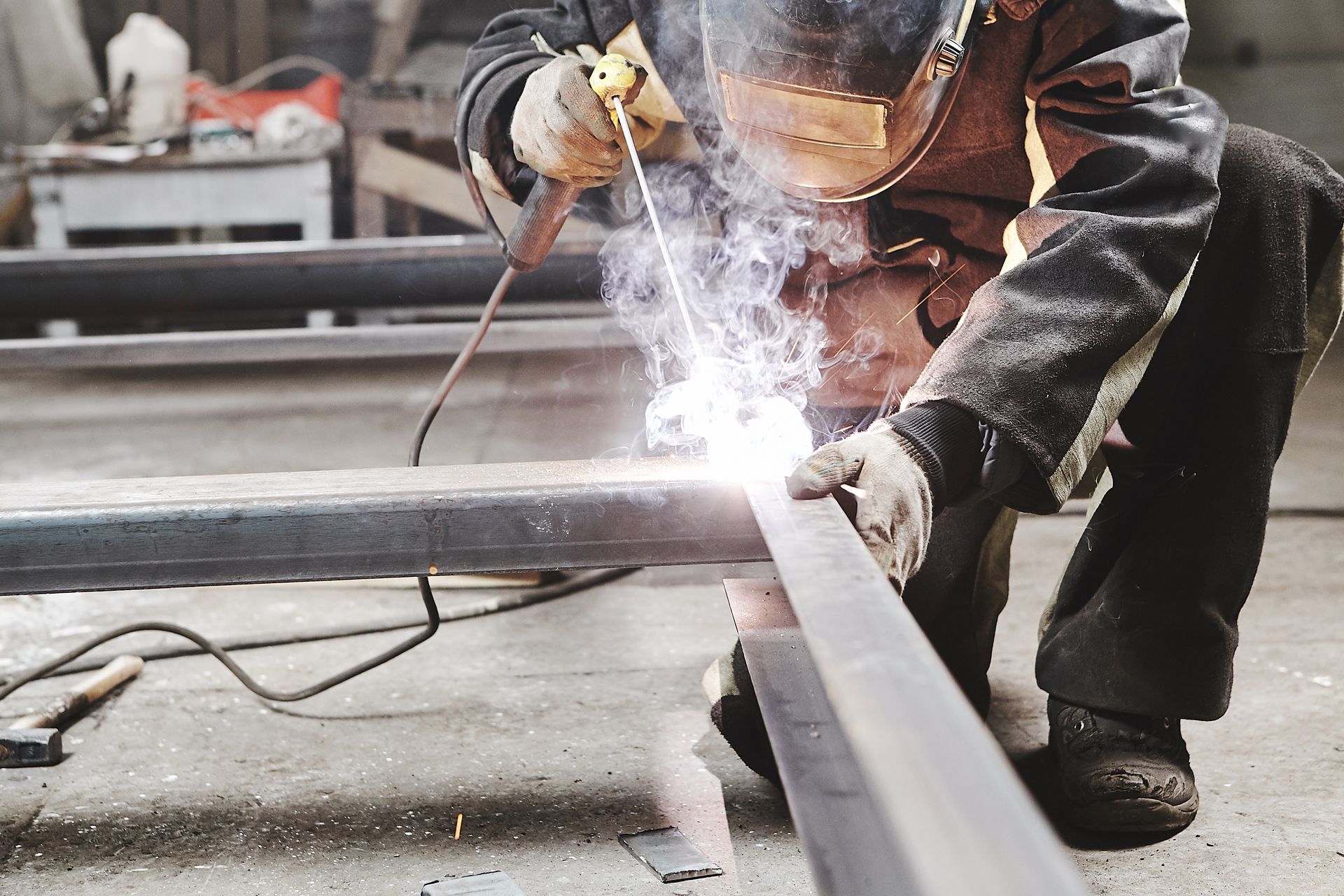 Worker welding metal beams with sparks in an industrial workshop