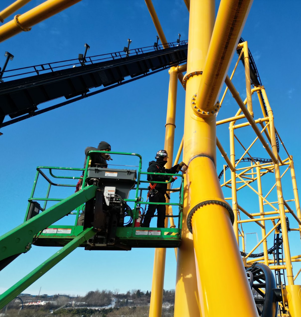 A man in a green cage is working on a yellow structure A man in a green cage is working on a yellow structure