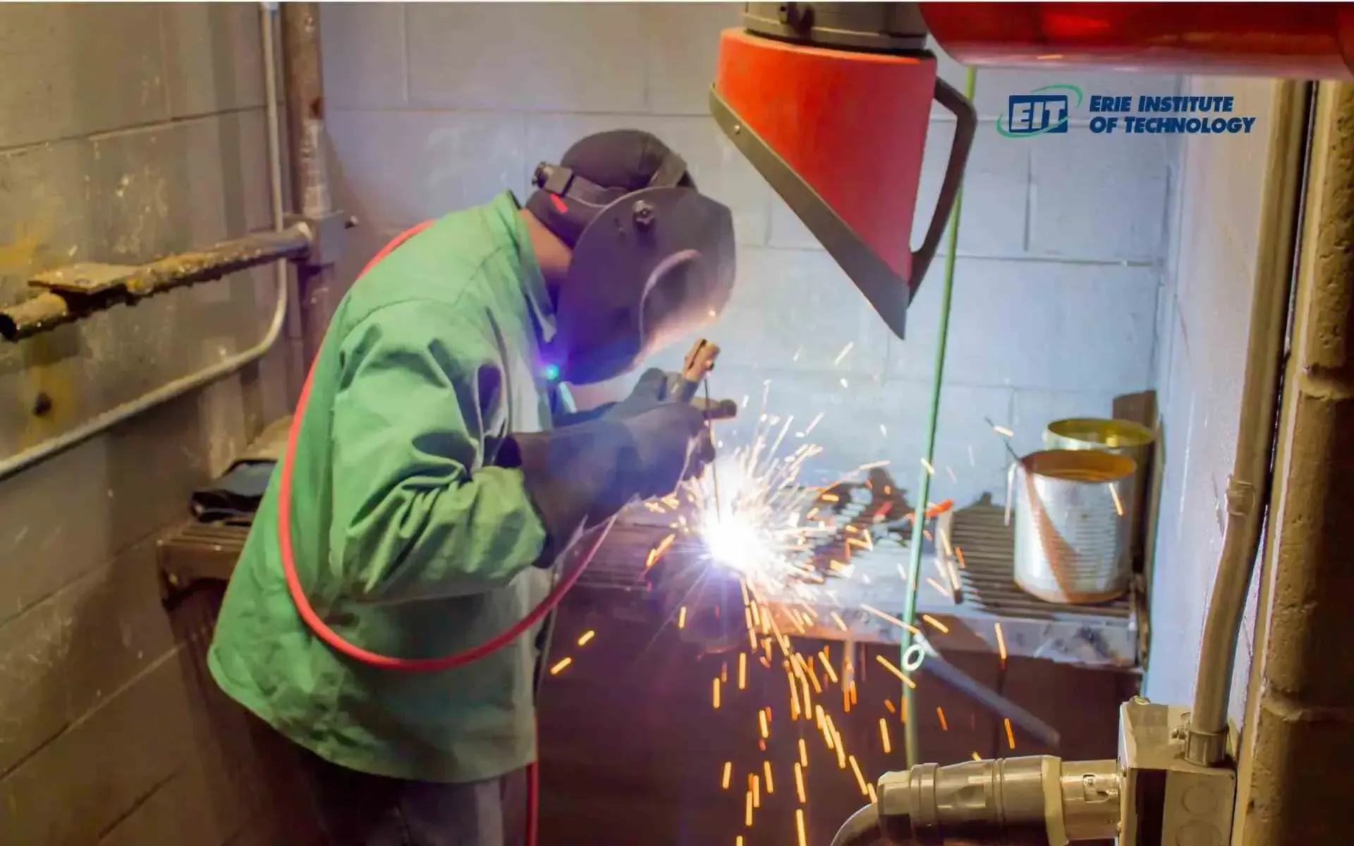 A man wearing a welding mask is welding a piece of metal