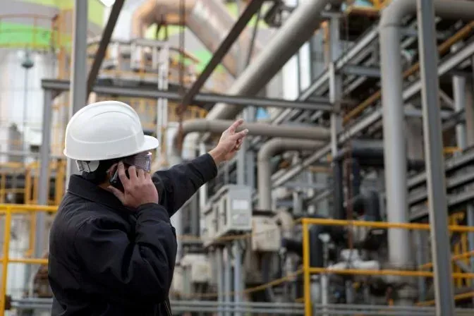 A man in a hard hat is talking on a cell phone in front of a factory. A man in a hard hat is talking on a cell phone in front of a factory.