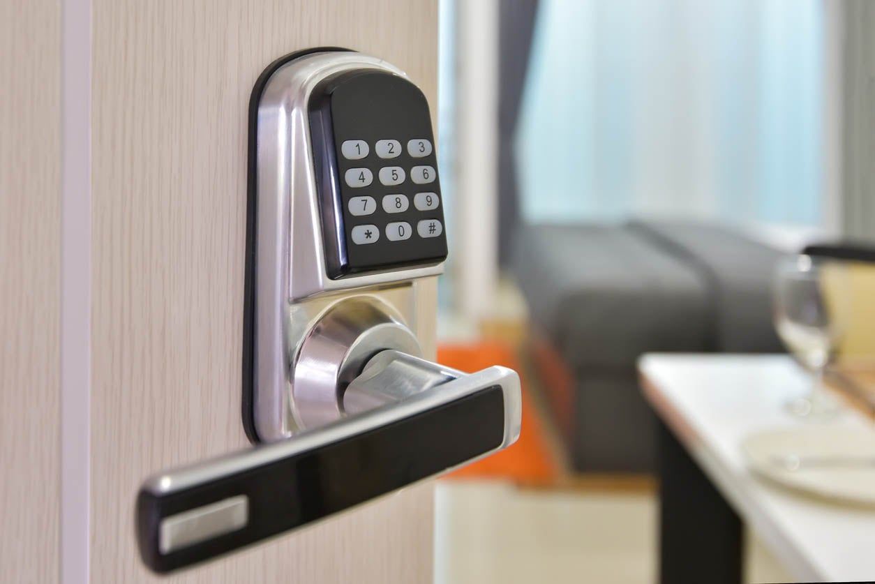 Silver digital keypad door lock on a light wooden door. Interior in the background.