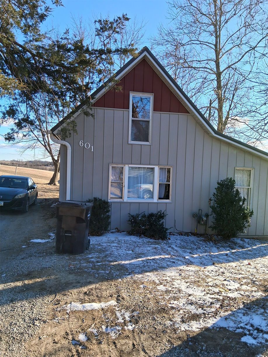 Small beige house with red gable roof, snow on the ground, and a parked car to the left.