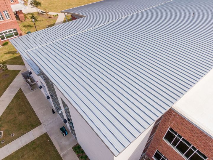 Aerial view of a large white metal roof on a brick building with nearby walkways and grass.