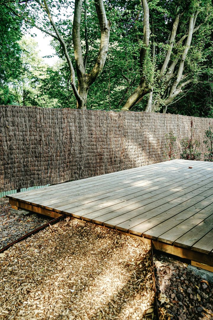 Wooden deck beside a woven fence, with trees and greenery in the background.