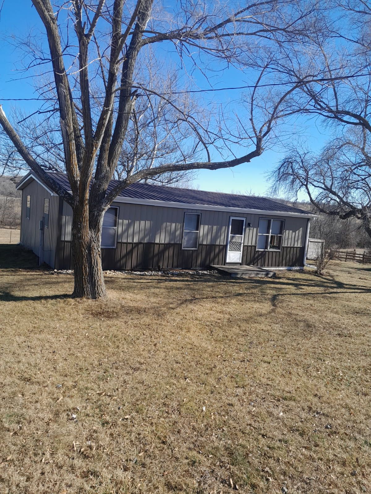 Single-story gray house with a white door and leafless trees in a winter yard