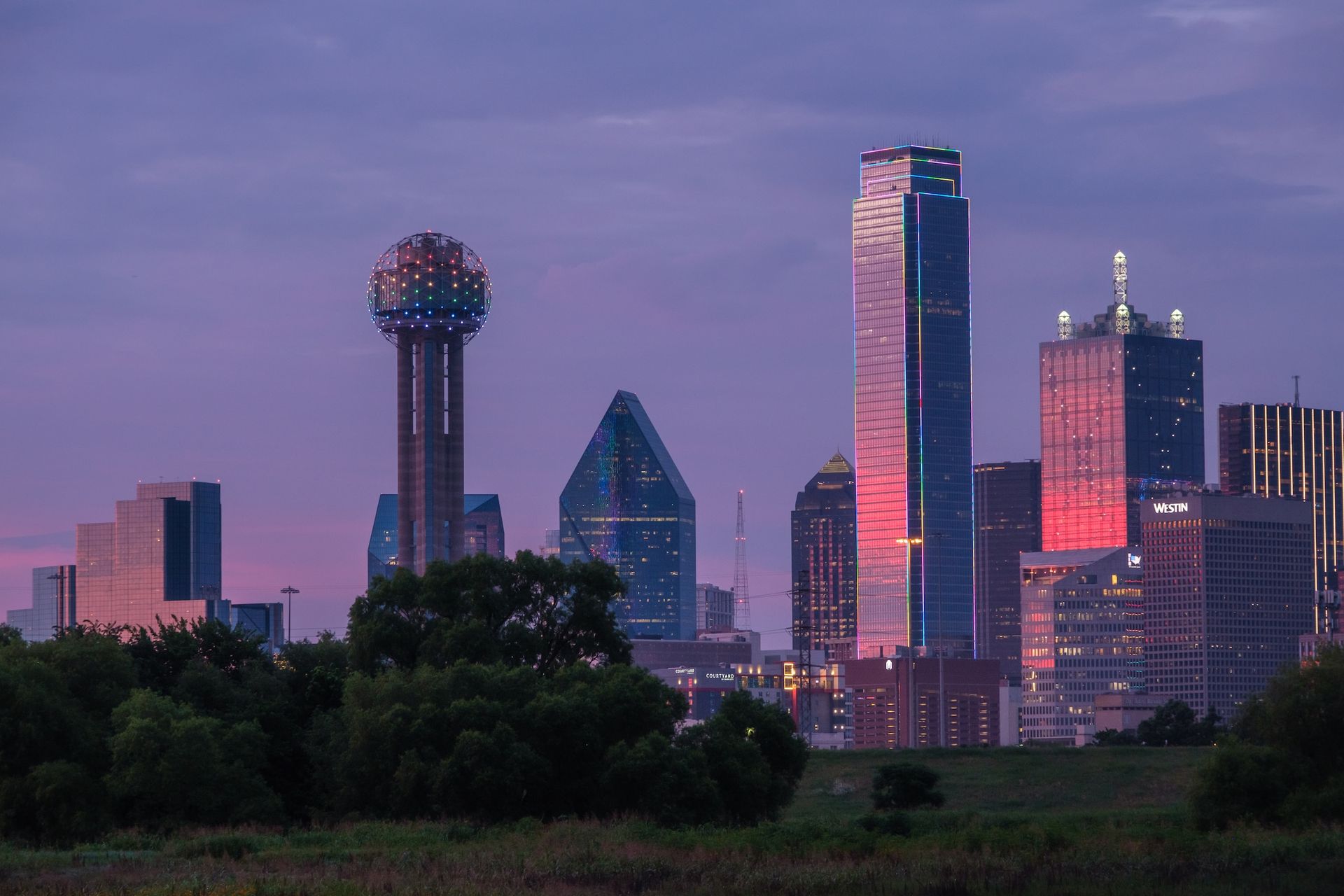 A view of the dallas skyline at night with a purple sky in the background.
