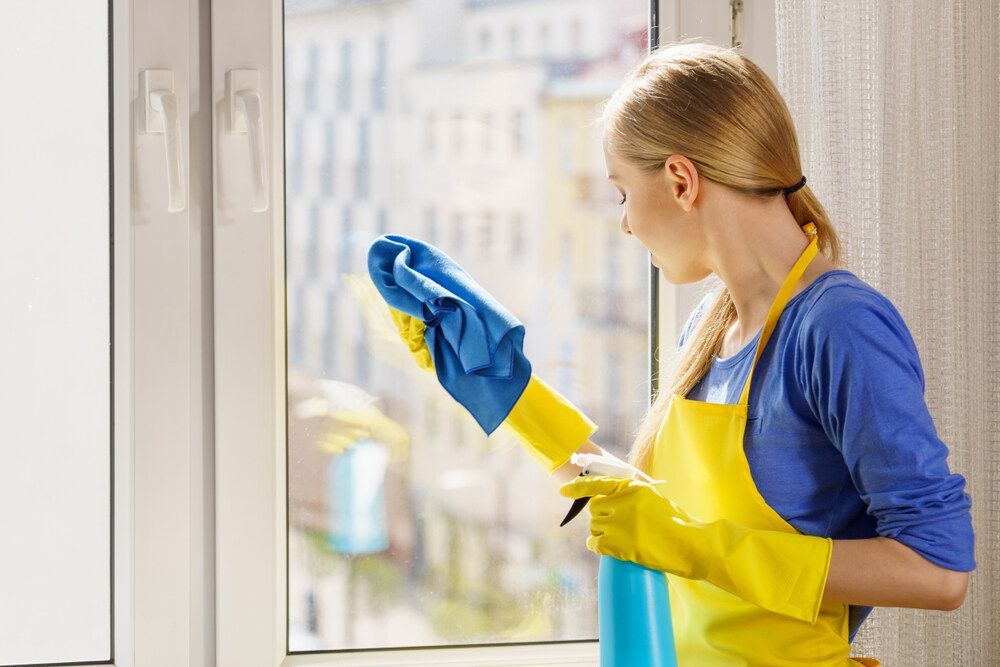 Woman is Cleaning a Window With a Cloth and Spray Bottle — Abstract Window Cleaning in Murwillumbah, NSW
