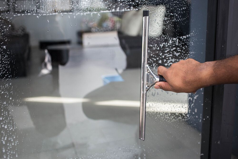 Person is Cleaning a Glass Door With a Squeegee — Abstract Window Cleaning in Kingscliff, NSW