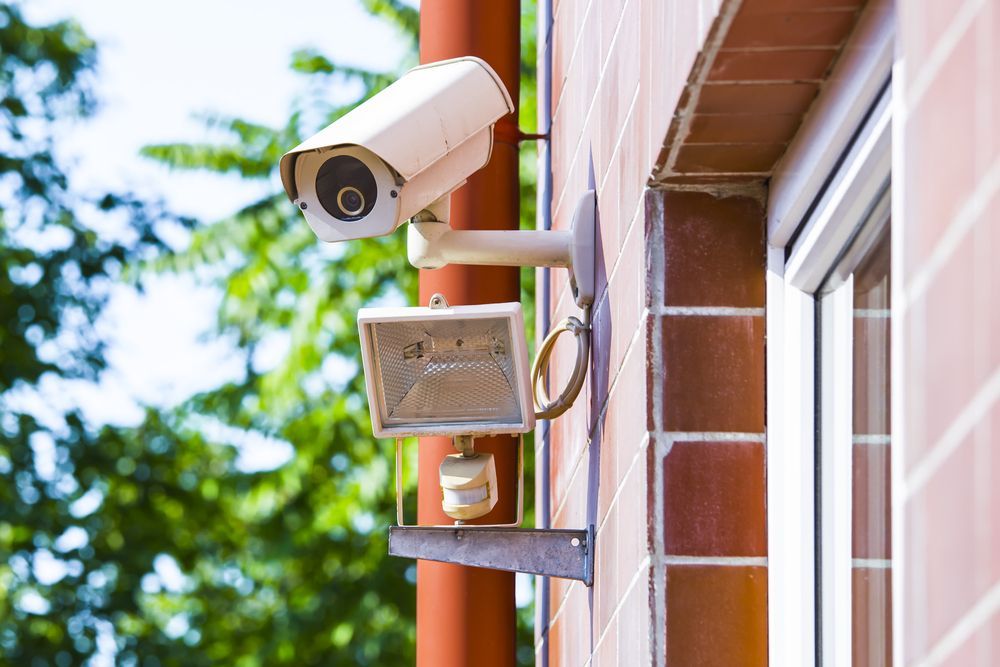 Security Camera and Floodlight Mounted on a Brick Building — Shaine Hunter Locksmiths in Camooweal, QLD
