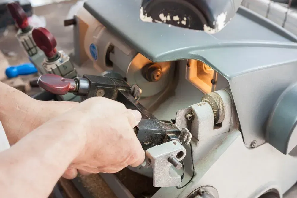 Hands Cutting a Key on a Key Duplicating Machine. Machine is Gray — Shaine Hunter Locksmiths in Normanton, QLD