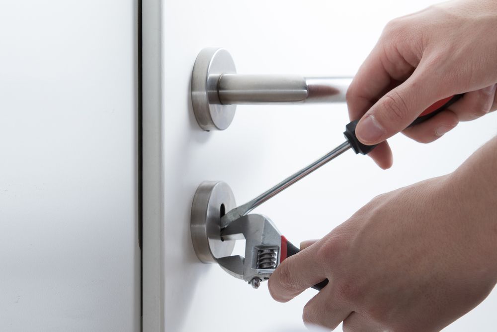 Hands Using Screwdriver and Wrench to Repair a Door Lock — Shaine Hunter Locksmiths in Doomadgee, QLD