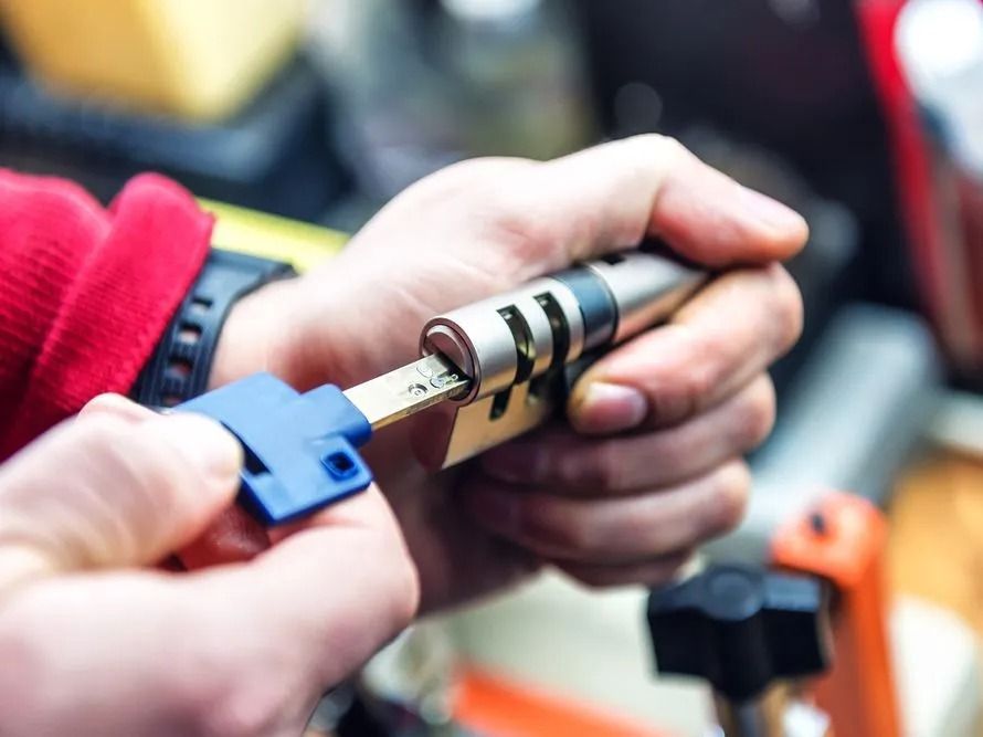 Hands Inserting a Blue Key Into a Silver Lock Cylinder — Shaine Hunter Locksmiths in Mount Isa City, QLD