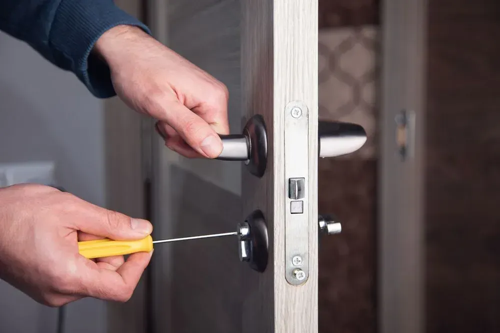 Person Using a Screwdriver to Adjust a Silver Door Handle on a White Door — Shaine Hunter Locksmiths in Mount Isa City, QLD