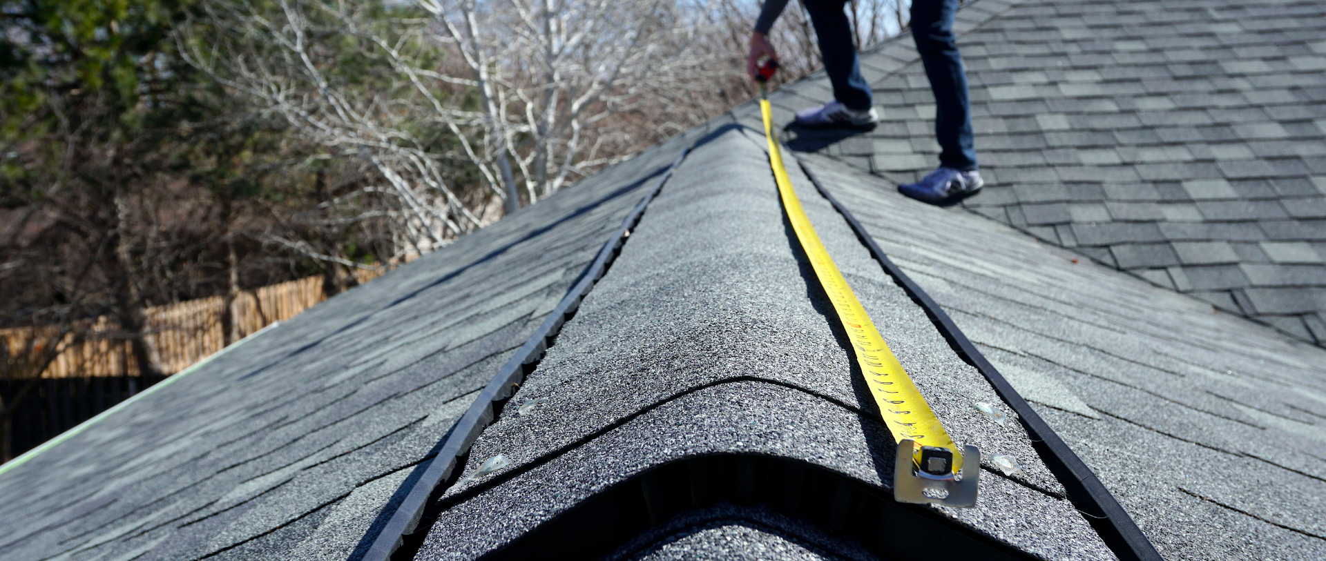 A person is measuring a roof with a tape measure.