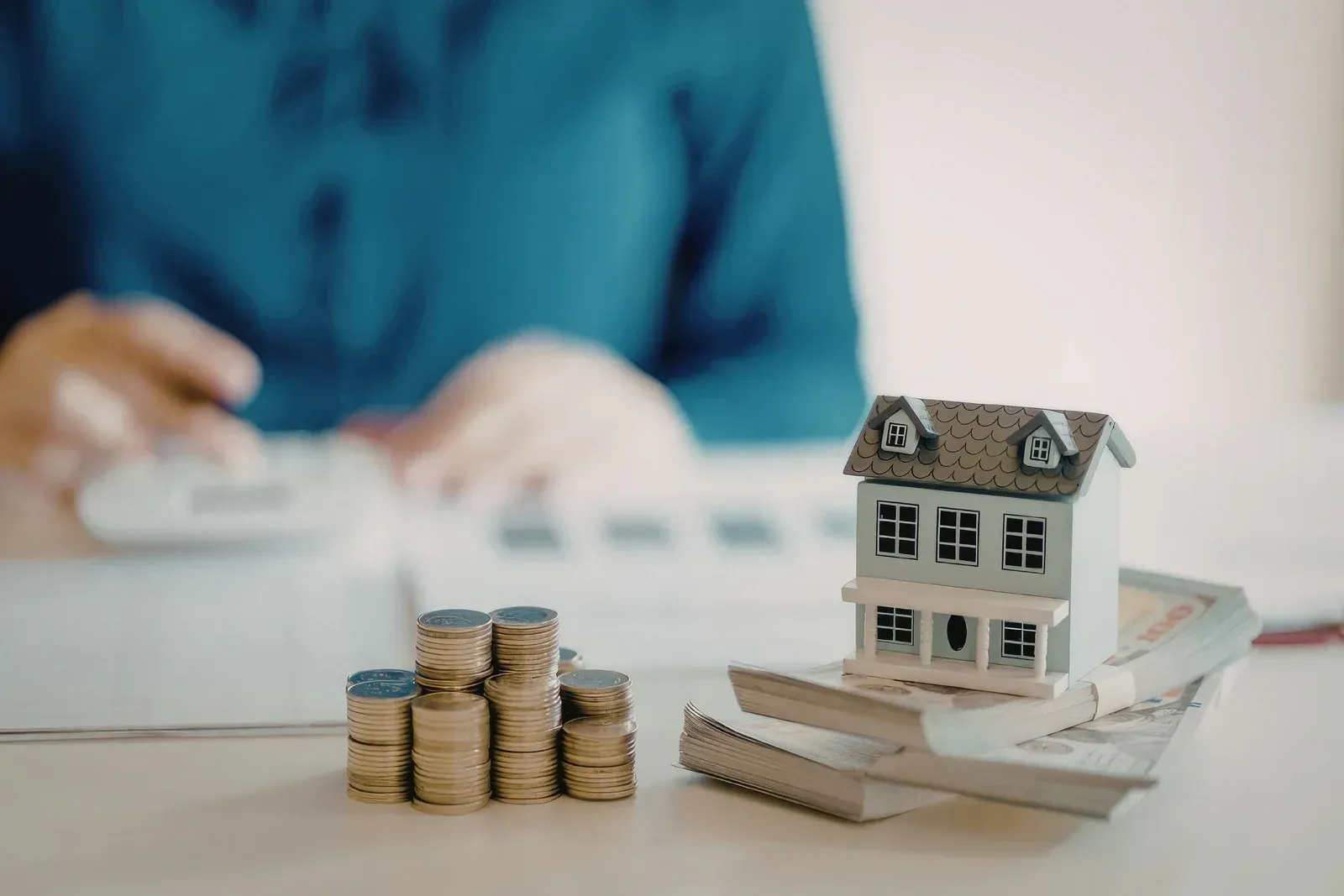 Miniature house on stacked coins with a blurred person in the background