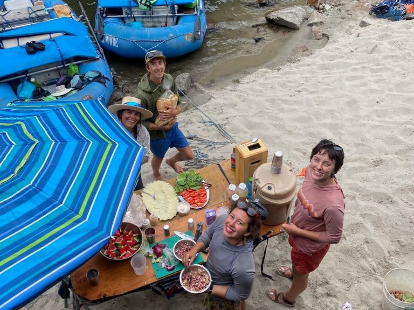 People gathered around a table with food and a striped umbrella.