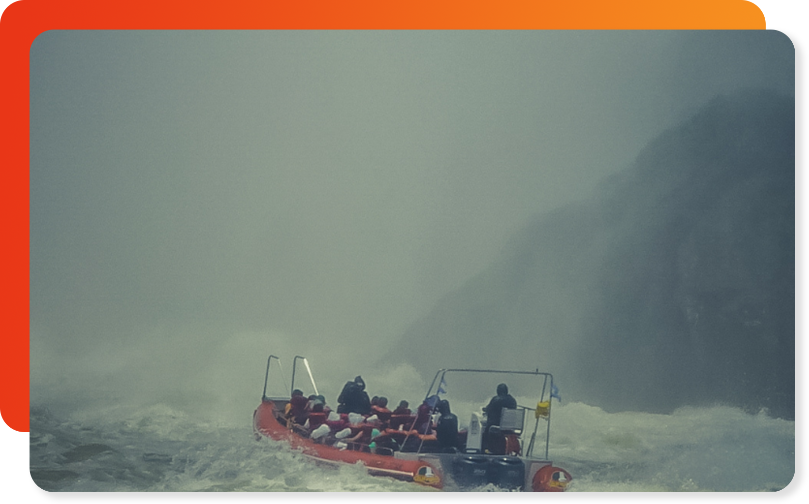 A red boat carrying several people navigating through rough, misty water near a large waterfall.