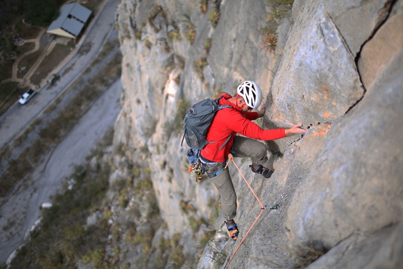 Rock climber in a red jacket scaling a steep cliff with a rope and backpack