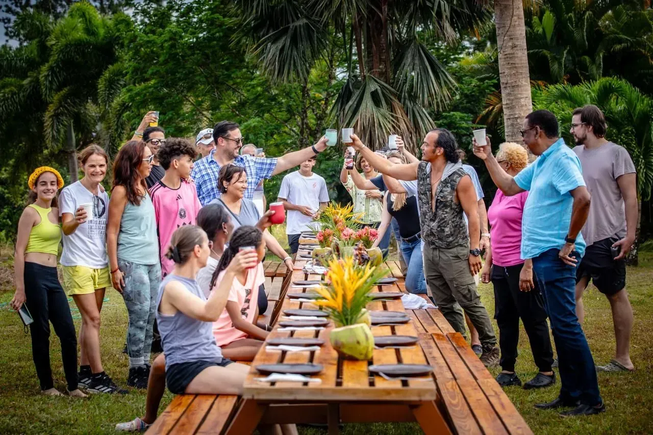 A group of people are standing around a long wooden picnic table.