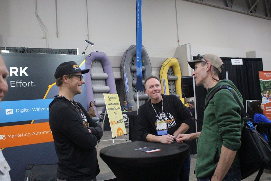 Three people chatting at a trade show booth with colorful tube displays and black cocktail tables